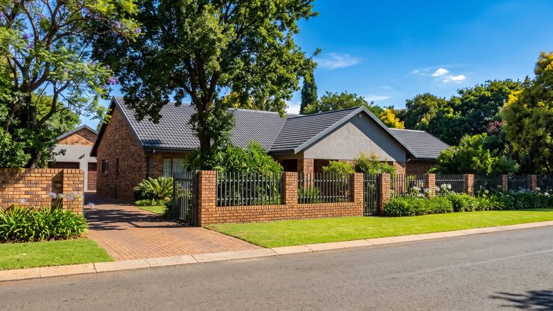 A face-brick home with a grey tiled roof on a tree-lined Johannesburg street.